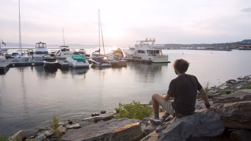 Un hombre se sienta al lado de un río, mirando los barcos.