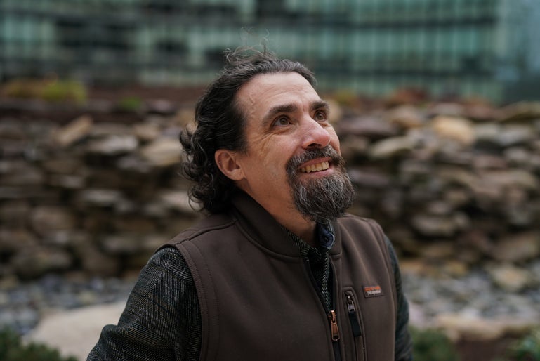 un hombre con barba, bigote y pelo oscuro. está mirando hacia arriba y parece contento.