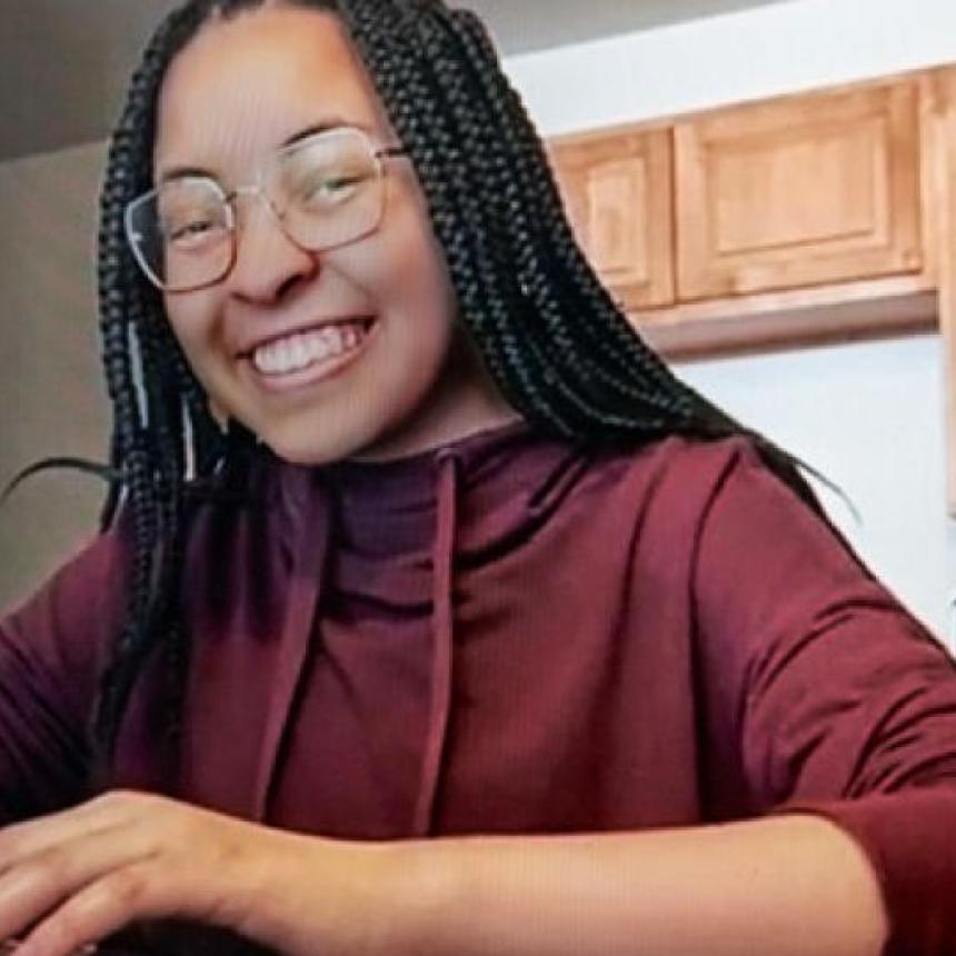 Una mujer con trenzas negras usa una computadora y sonríe