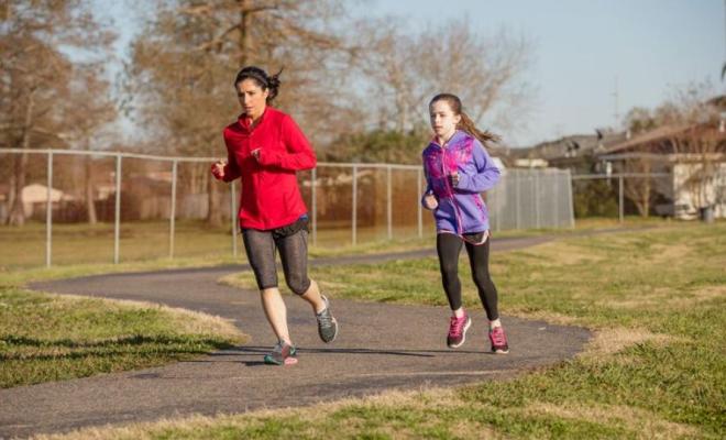 Un adulto y una niña corren juntos sobre un sendero en un parque