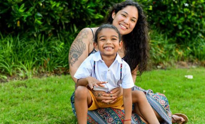 Una madre abraza a un niño. Los dos están sentados en un parque sobre el césped.