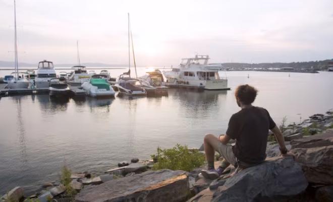Un hombre se sienta al lado de un río, mirando los barcos.