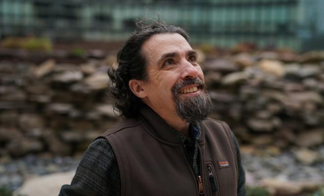 un hombre con barba, bigote y pelo oscuro. está mirando hacia arriba y parece contento.