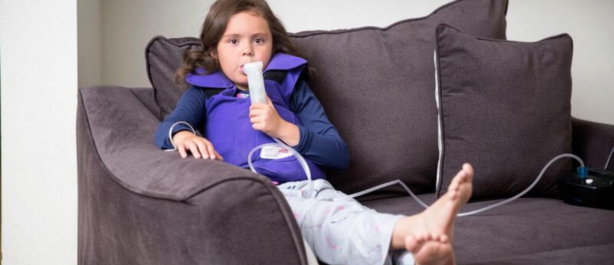 Una niña respira por medio de un nebulizador mientras lleva un chaleco de presión positiva externa
