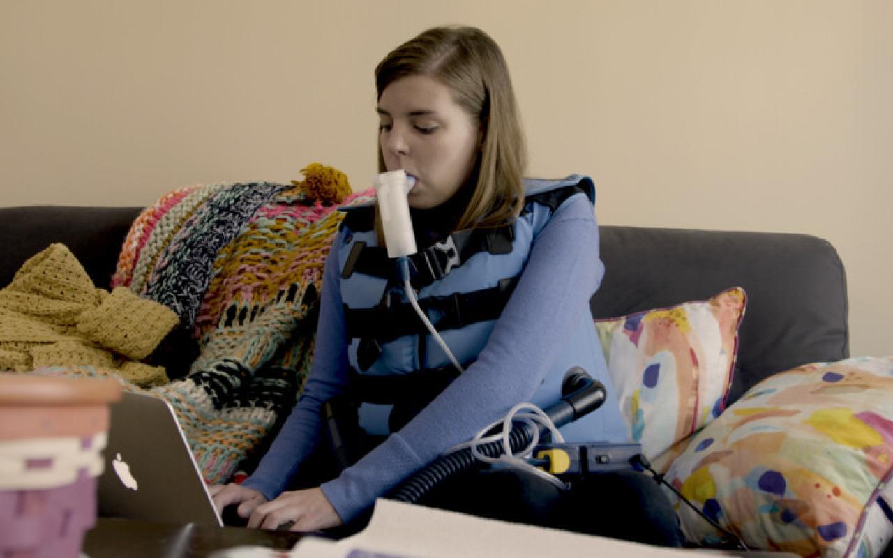 Un adulto con FQ lleva un chaleco mientras usa su nebulizador para limpiar las vías respiratórias
